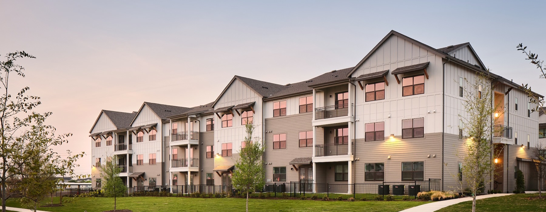 a row of apartments at dusk with a walkway and grass
